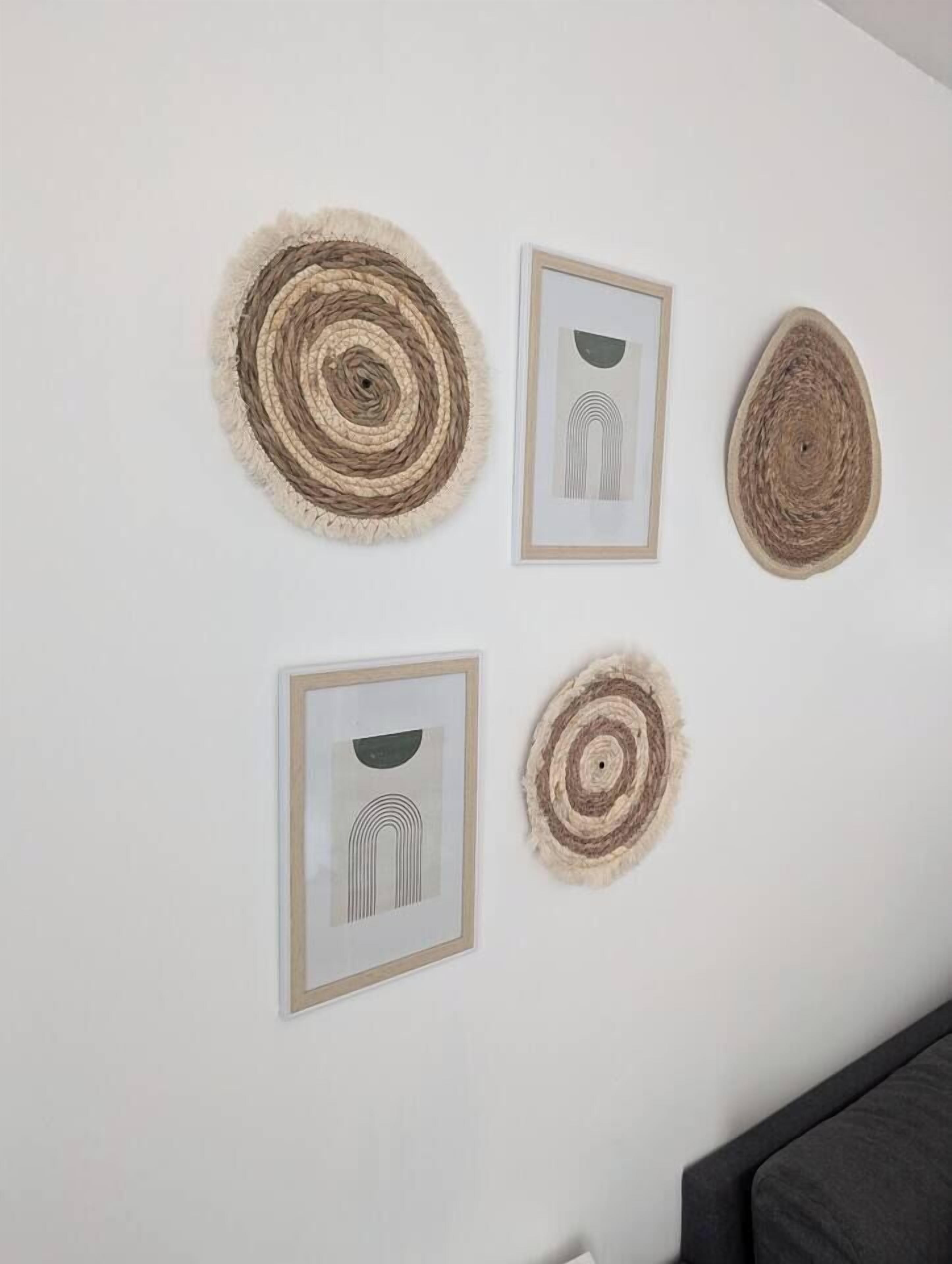A white wall with four framed artworks and two woven wall hangings.