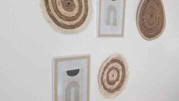 A white wall with four framed artworks and two woven wall hangings.