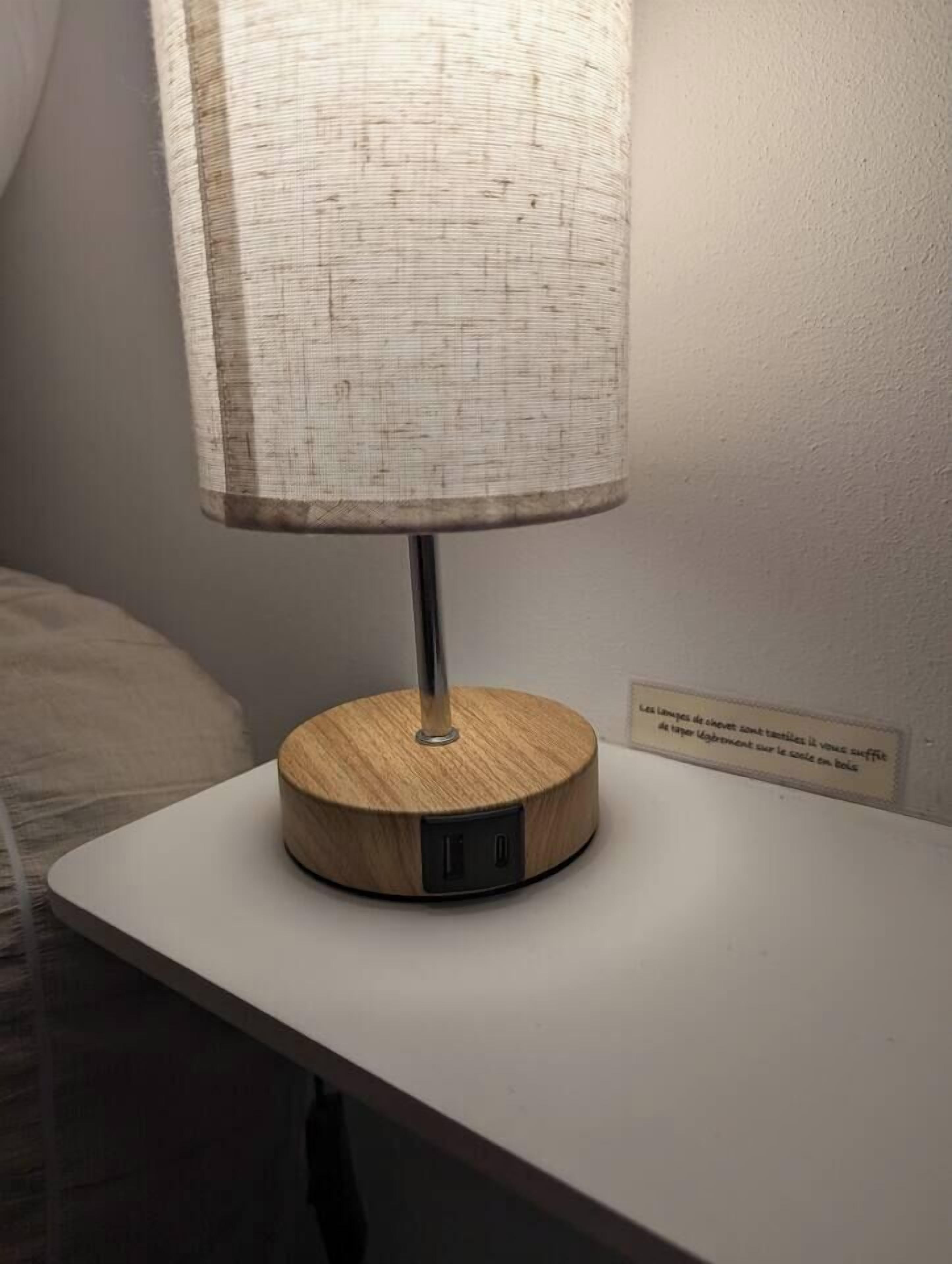 Een tafellamp met houten voet en stoffen kap op een witte tafel.