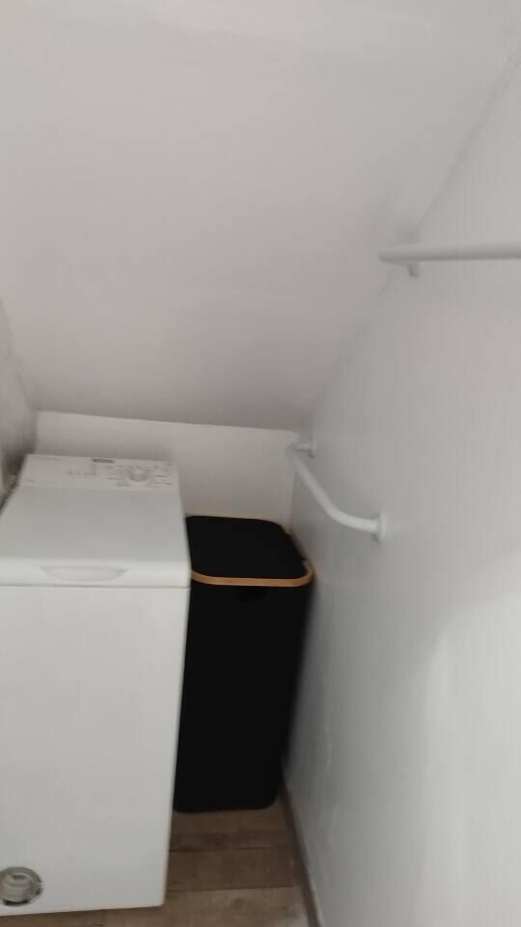 A small, narrow bathroom with a white toilet and a black trash bin.
