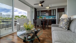 A modern living room with a glass coffee table, a grey sofa, and a dining area with dark wooden furniture. - Heart of Waikiki, 2 blocks to beach, kitchenette, lanai, free parking nearby! (Honolulu)