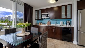 A modern kitchen with dark wooden cabinets, a stainless steel refrigerator, and a glass dining table with a vase of flowers. - Heart of Waikiki, 2 blocks to beach, kitchenette, lanai, free parking nearby! (Honolulu)