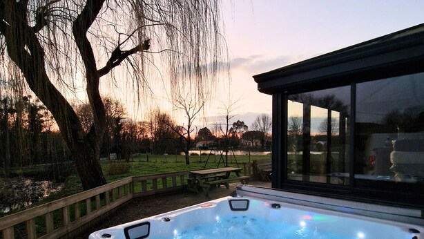 A hot tub with a wooden deck and a view of a park with trees and a picnic table. - Grand gîte Le saule en scie - SPA - Ideal 12 to 14 pers - Group family friends pro (Nueil-les-Aubiers)