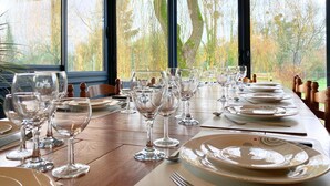 A dining table set with multiple wine glasses and plates, positioned in a room with large windows offering a view of trees and a wooden deck outside. - Grand gîte Le saule en scie - SPA - Ideal 12 to 14 pers - Group family friends pro (Nueil-les-Aubiers)