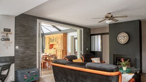 A modern living room with a black velvet sofa, wooden chairs, a dining area, and a fireplace. - Grand gîte Le saule en scie - SPA - Ideal 12 to 14 pers - Group family friends pro (Nueil-les-Aubiers)