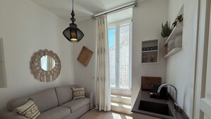 Um apartamento moderno com sofá, luminária pendente, área de cozinha e vista pela porta deslizante.