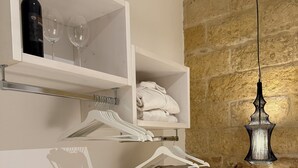 Uma casa de banho com parede de pedra, um candeeiro suspenso, uma estante com uma garrafa e copos, um porta-toalhas e uma pequena mesa com um livro.