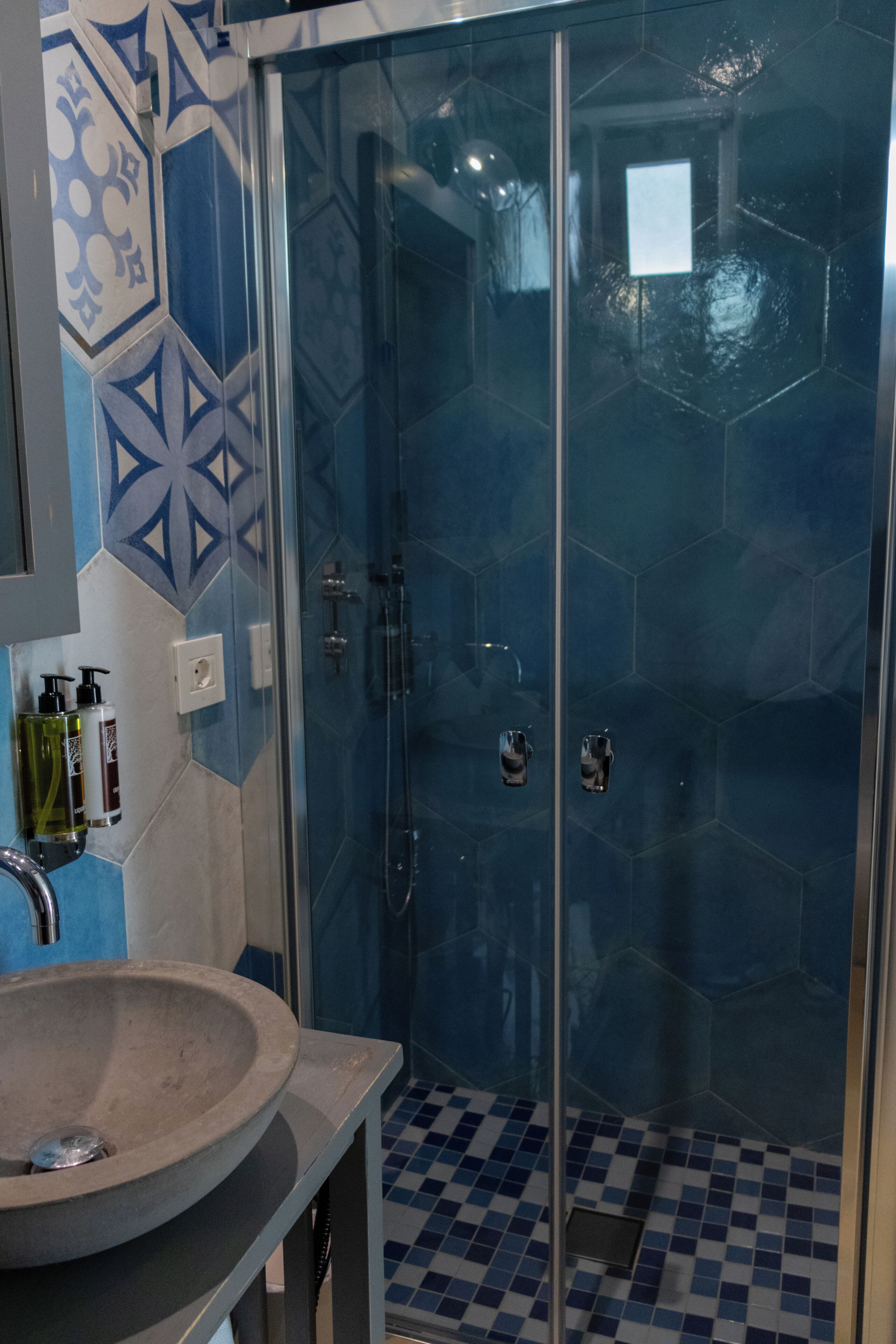 Un bany amb plat de dutxa tancat per vidre, un lavabo i rajoles amb disseny.