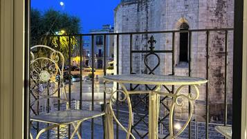A balcony with wrought iron furniture, a stone building with a clock tower in the background, and a clear night sky.
