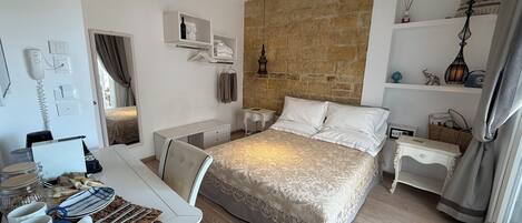 Un dormitorio con cama, mesitas de noche, un escritorio con silla, un armario y una pared de piedra.