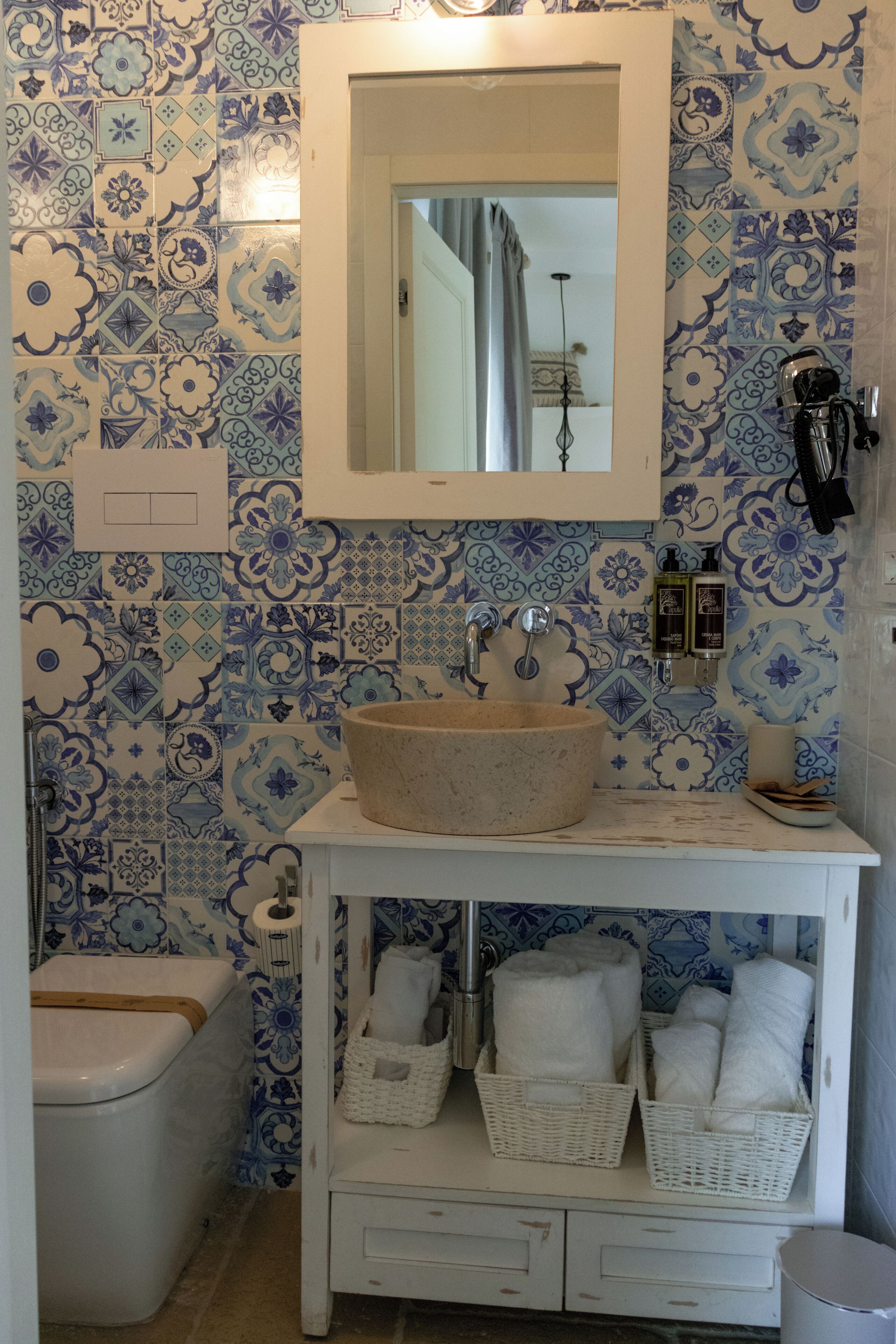 Un baño con un lavabo blanco, azulejos blancos y azules con estampado, un mueble blanco y un inodoro blanco.