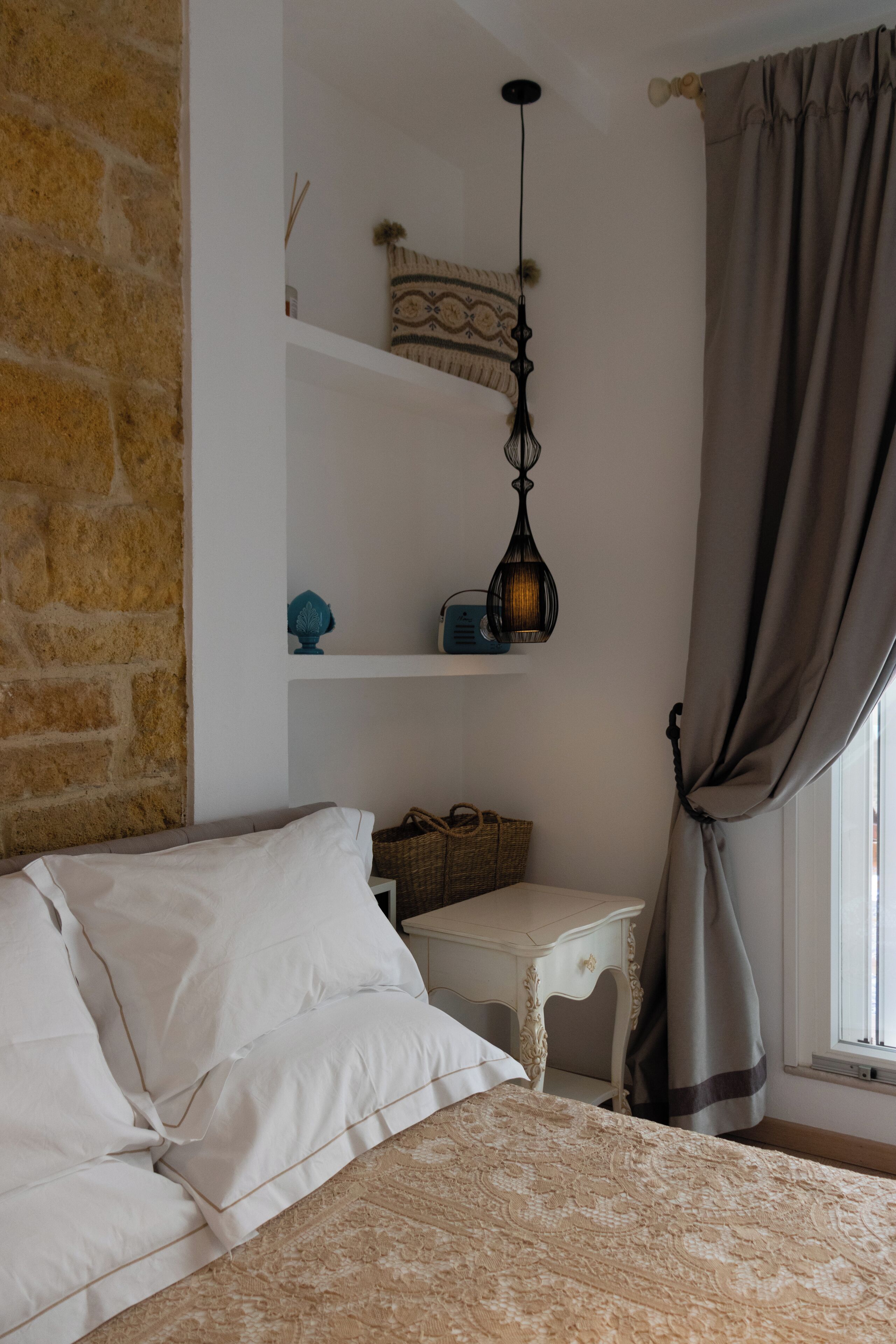 Un dormitorio con cama, mesita de noche, cómoda, ventana con cortinas y pared de ladrillo.