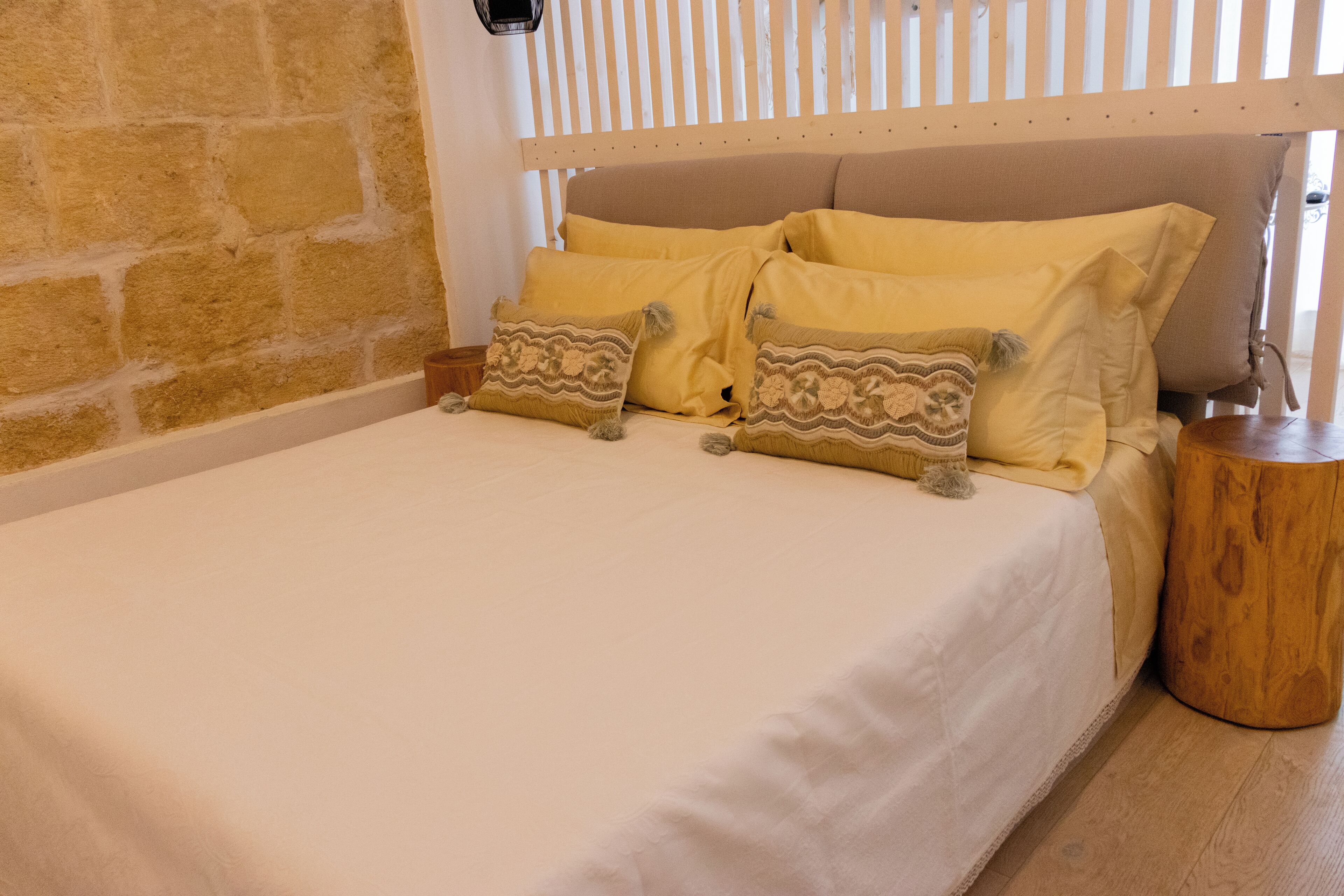Uma cama com cabeceira de madeira, parede de pedra e mesa de cabeceira de madeira.