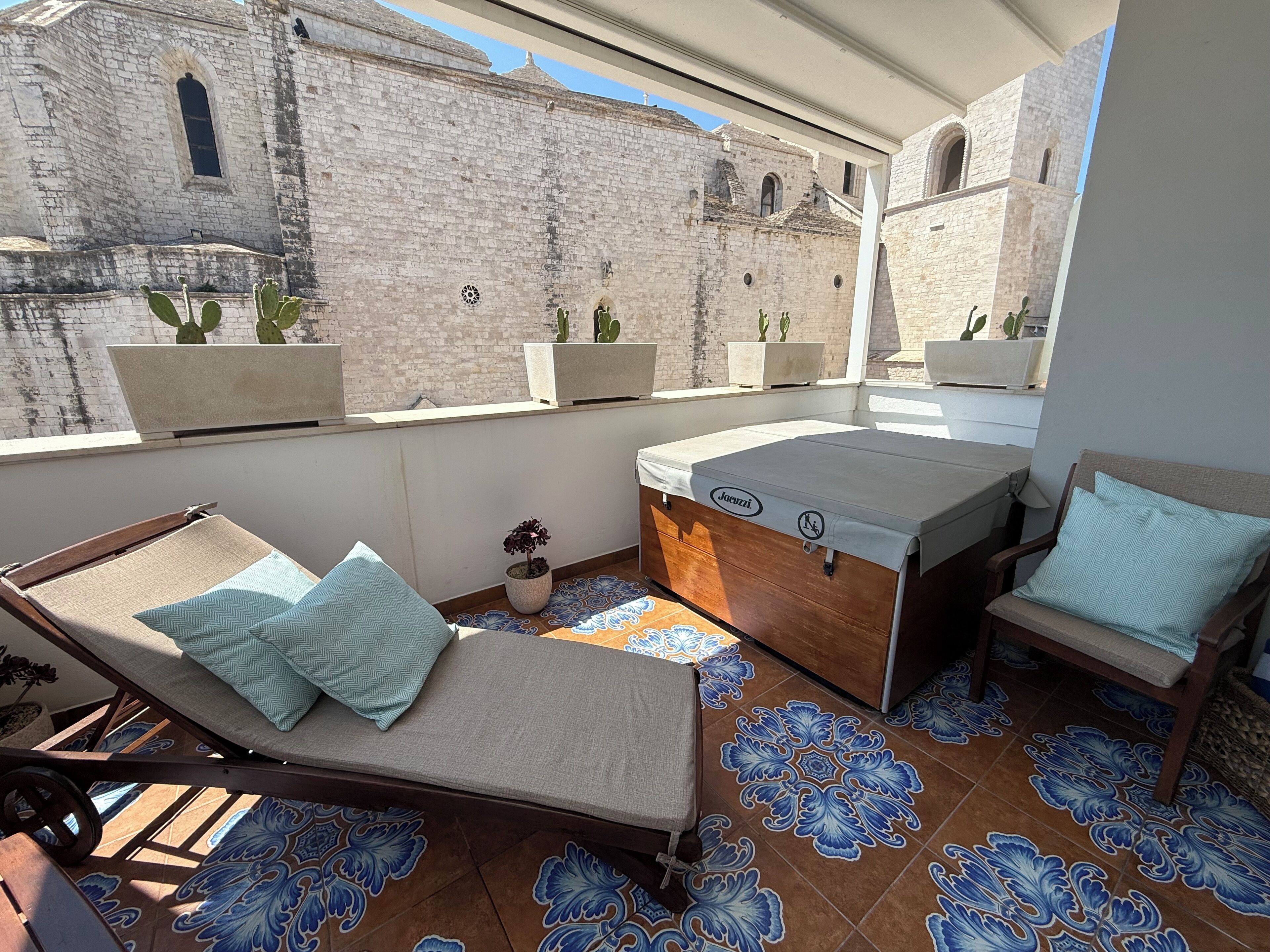 A rooftop terrace with a lounge chair, a small table, and a sofa. There are potted cacti on the terrace.