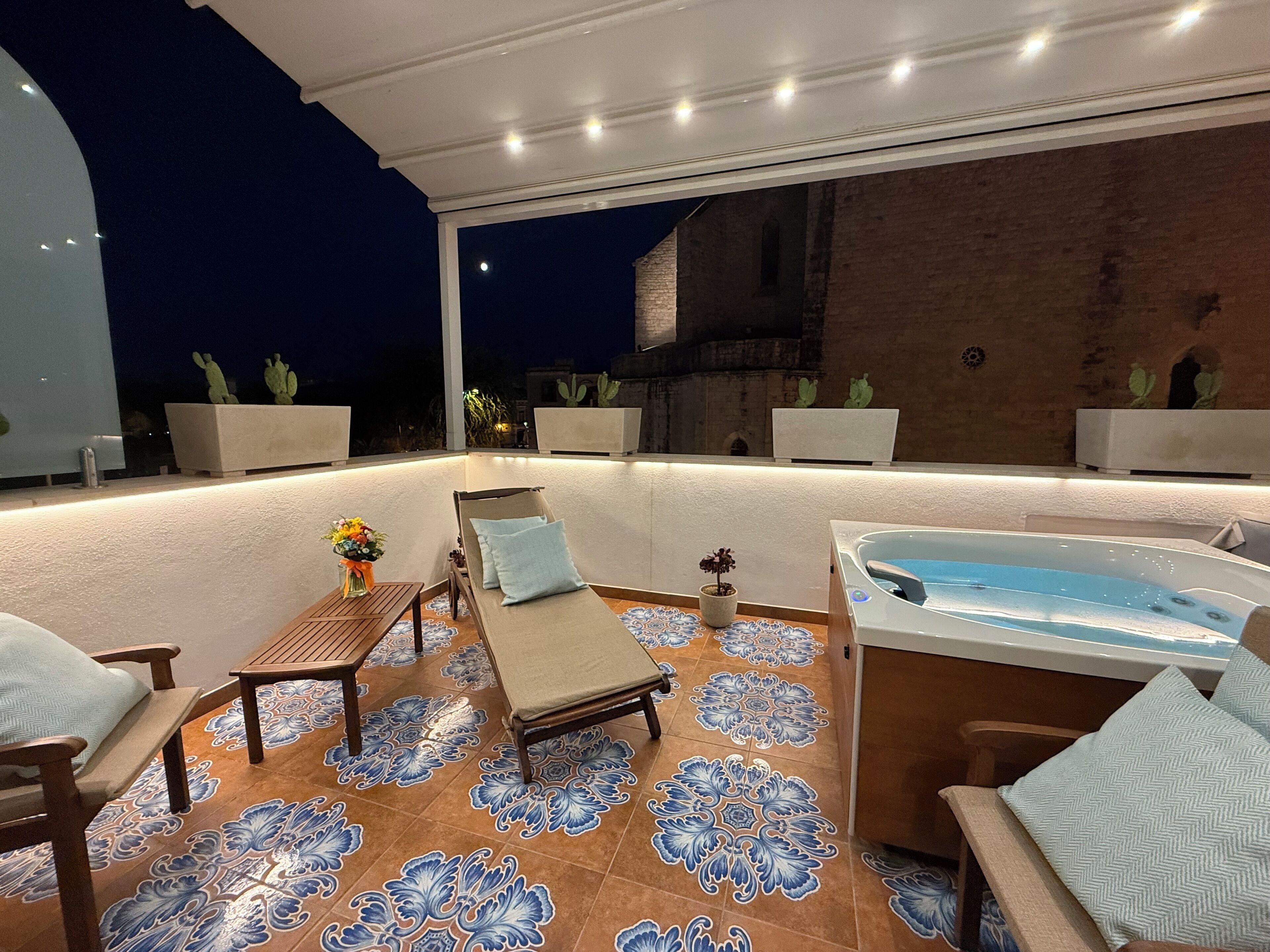 An outdoor patio with a hot tub, lounge chairs, and a decorative tiled floor.