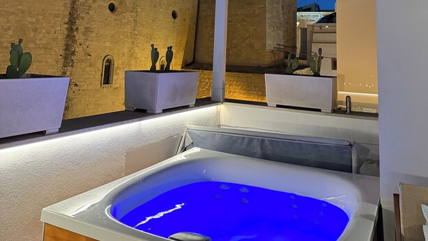 Terraço no telhado com banheira de hidromassagem, vista de um edifício histórico e uma torre com janelas iluminadas.