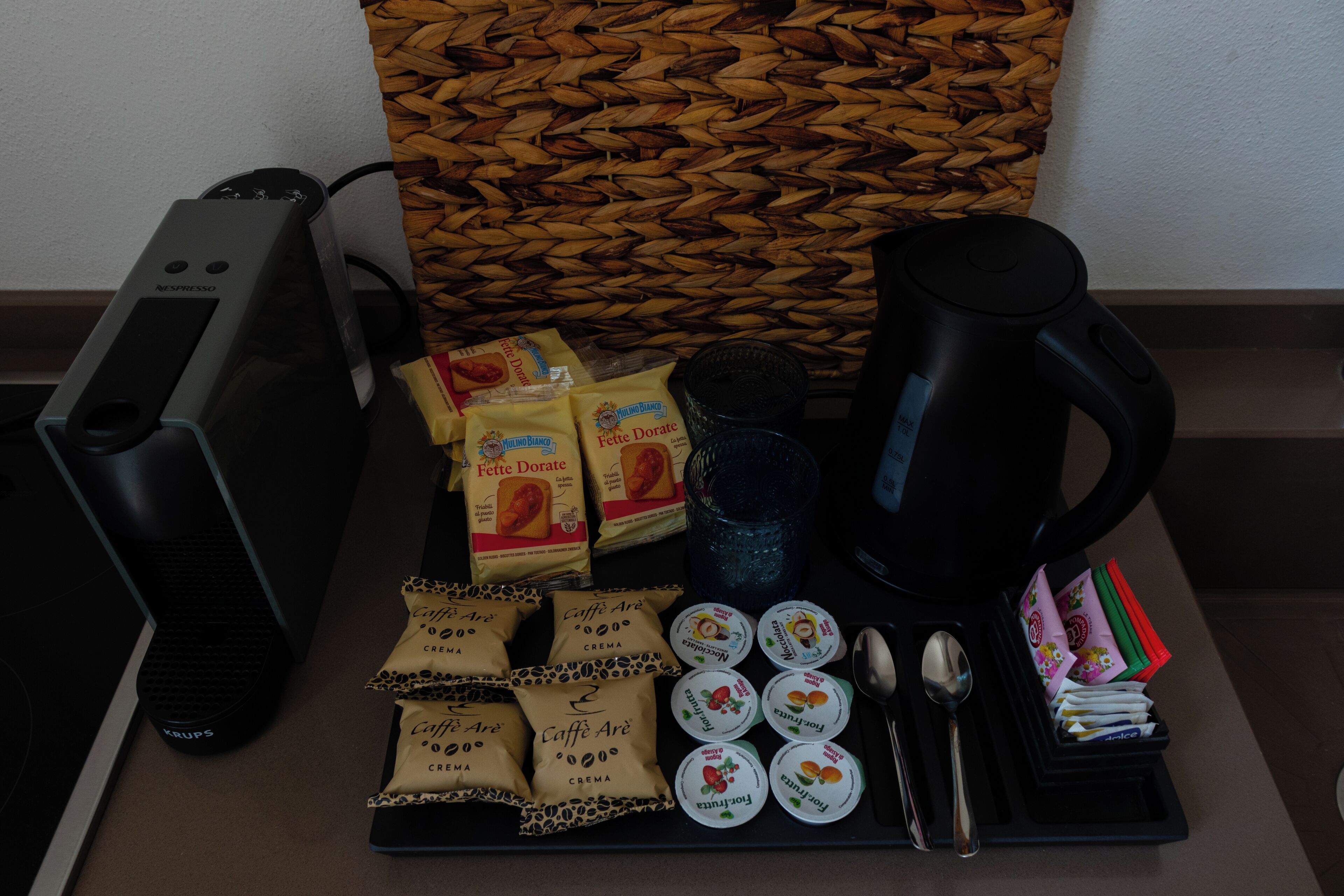Una estación de café con cafetera, tazas, sobres de crema y una cesta tejida.