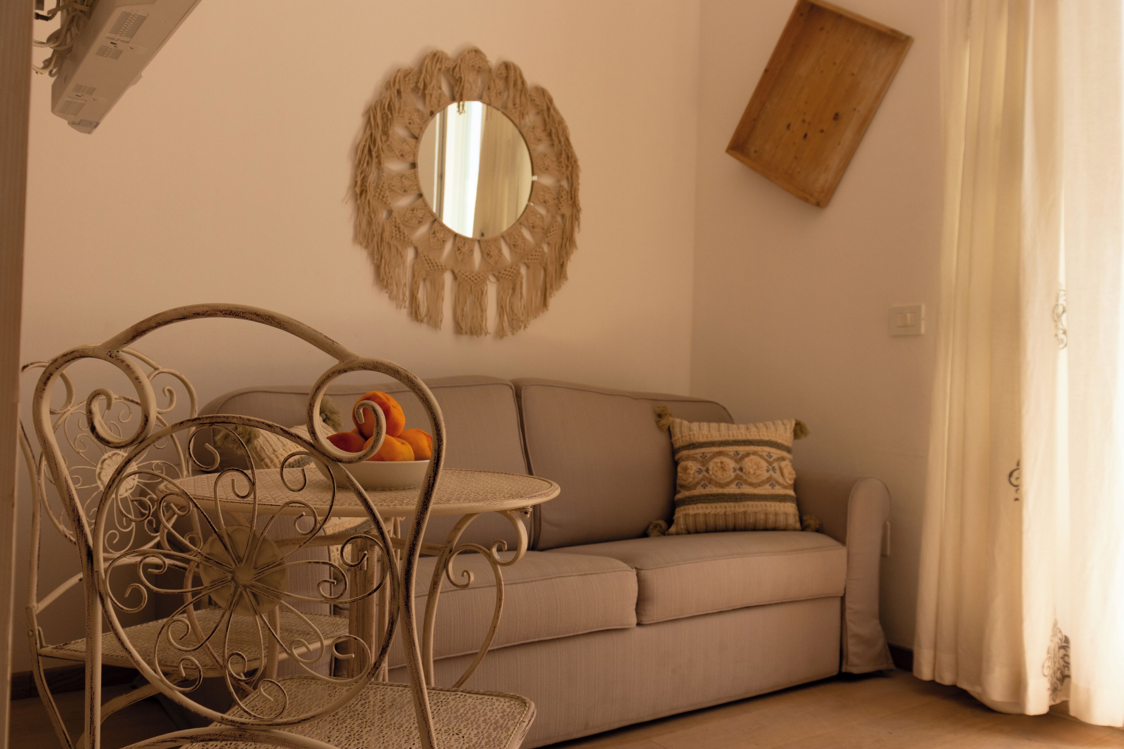 Un salon avec un canapé, un miroir rond, une chaise en métal et une table sur laquelle se trouvent des fruits.