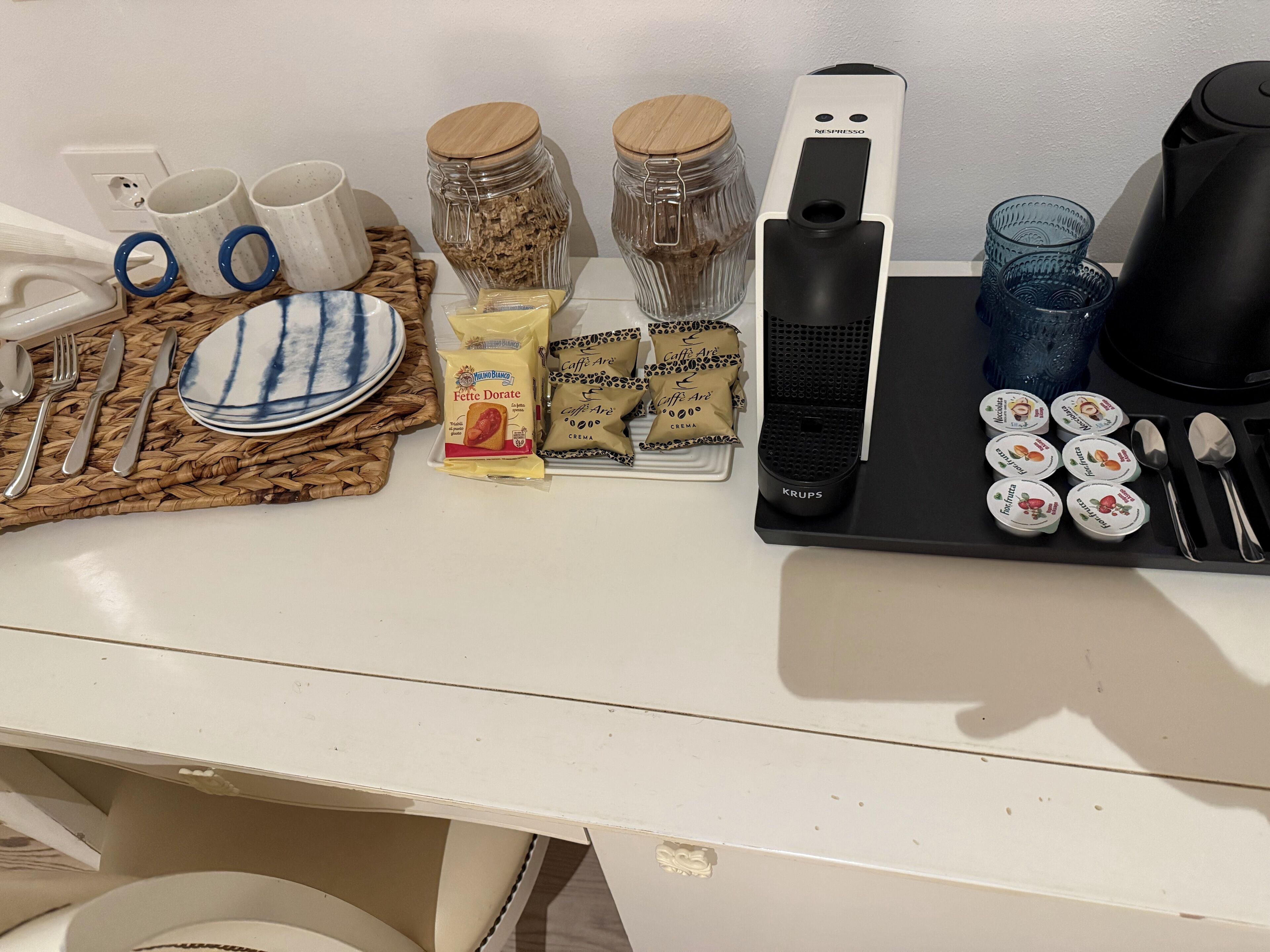 Eine Küchenarbeitsplatte mit verschiedenen Gegenständen, darunter eine Kaffeemaschine, Gläser, Tassen und Lebensmittelverpackungen.