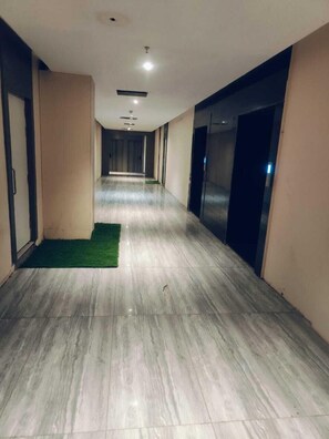 Un long couloir étroit, doté d’un sol en marbre, d’un éclairage encastré et d’une moquette verte à l’entrée.