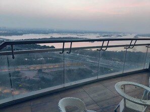 Uma varanda com vista para a cidade e para o rio. Há duas cadeiras de vime no chão.