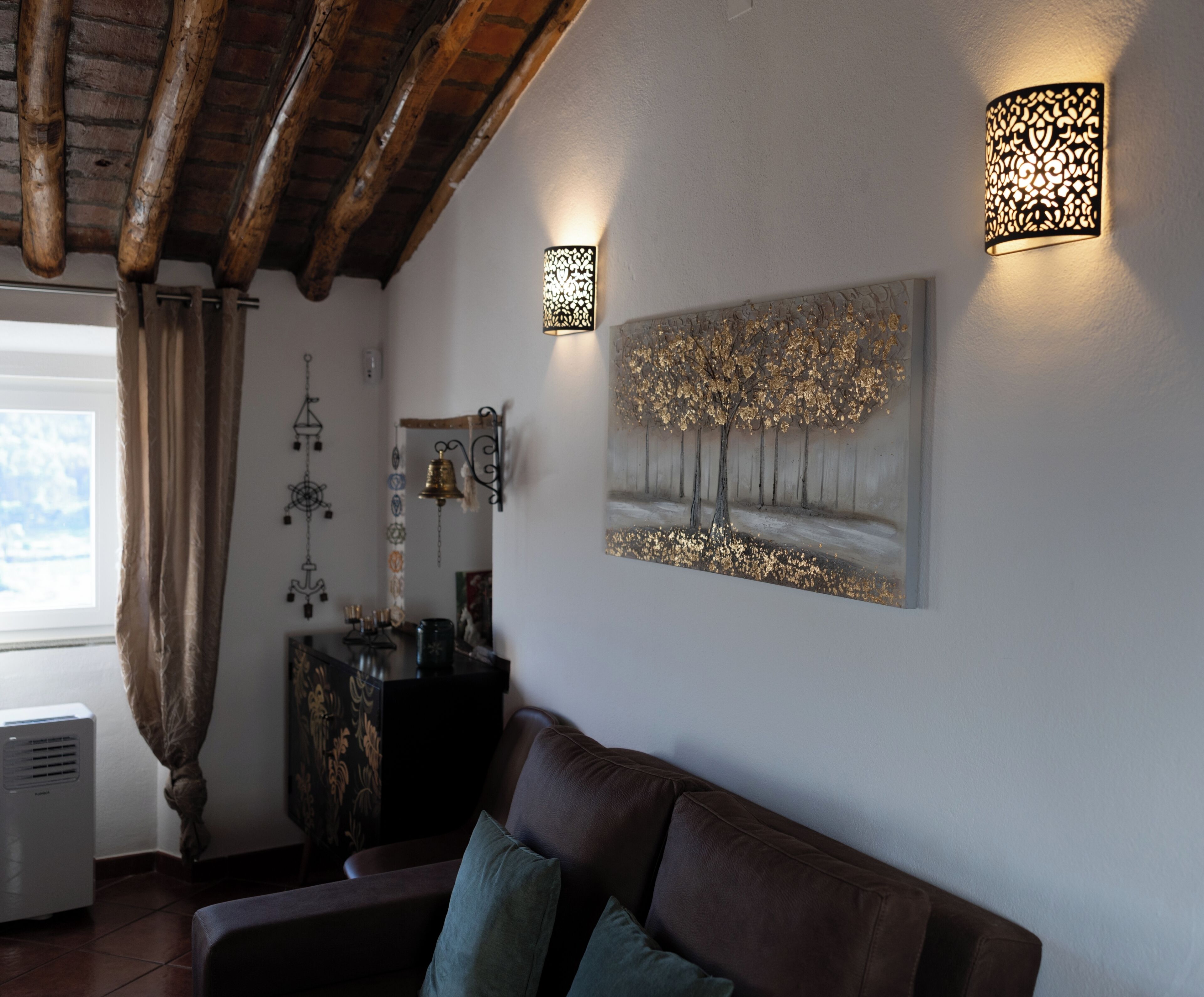Un salon avec un canapé en cuir marron, un tableau accroché au mur et deux appliques murales.