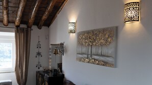 A living room with a brown leather sofa, a wall-mounted painting, and two wall sconces. - Encanto da Aldeia (Castelo de Vide)