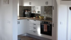 A kitchen with white cabinets, a microwave, oven, and a tiled backsplash. - Encanto da Aldeia (Castelo de Vide)