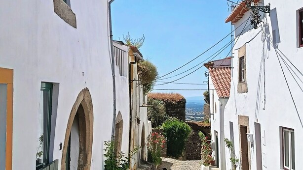 A narrow cobblestone street flanked by white buildings with arched doorways and tiled roofs. - Encanto da Aldeia (Castelo de Vide)