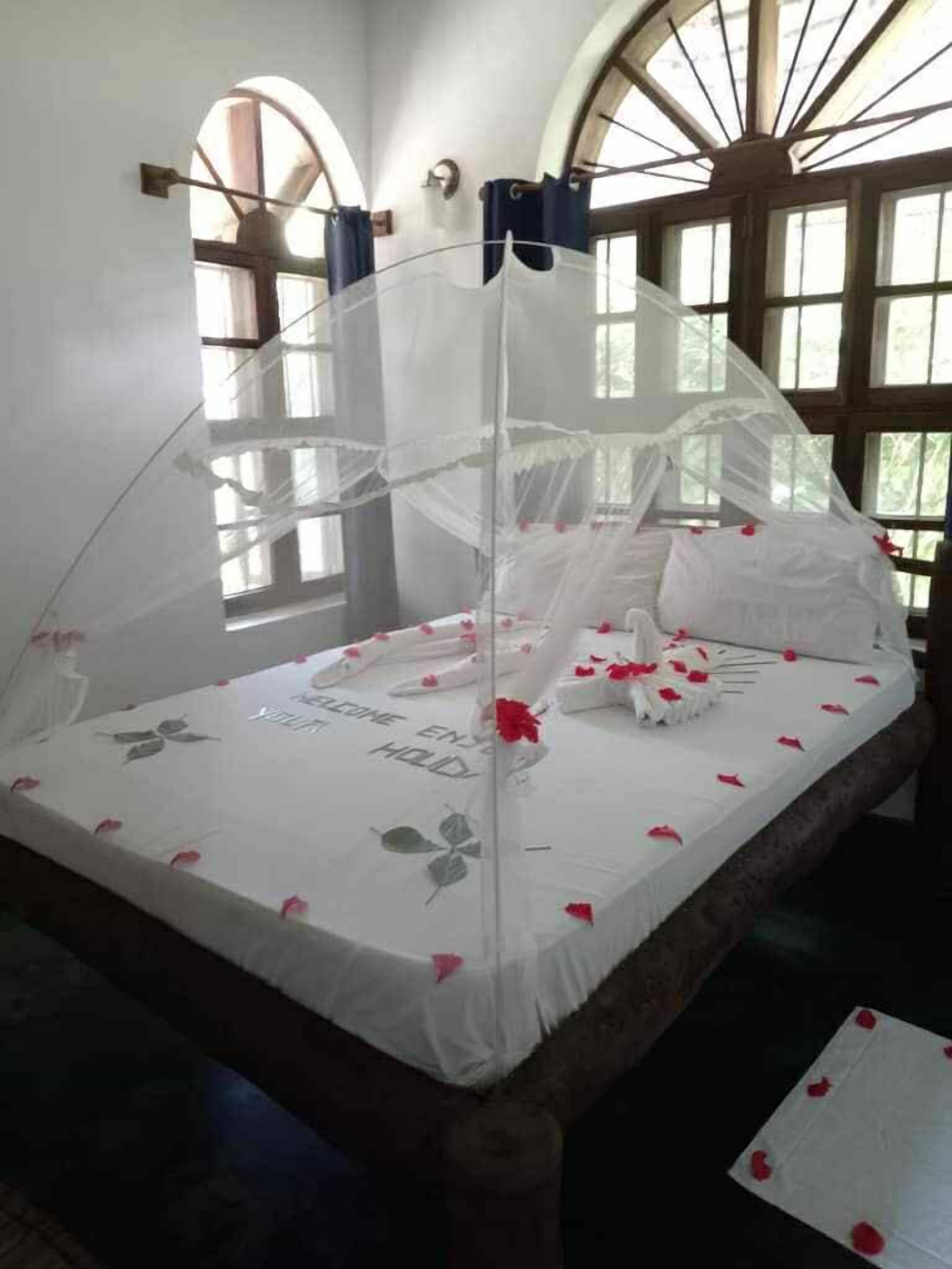 A bed with a canopy, white bedding, and red rose petals.