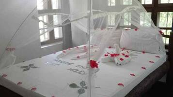 A bed with a canopy, white bedding, and red rose petals.