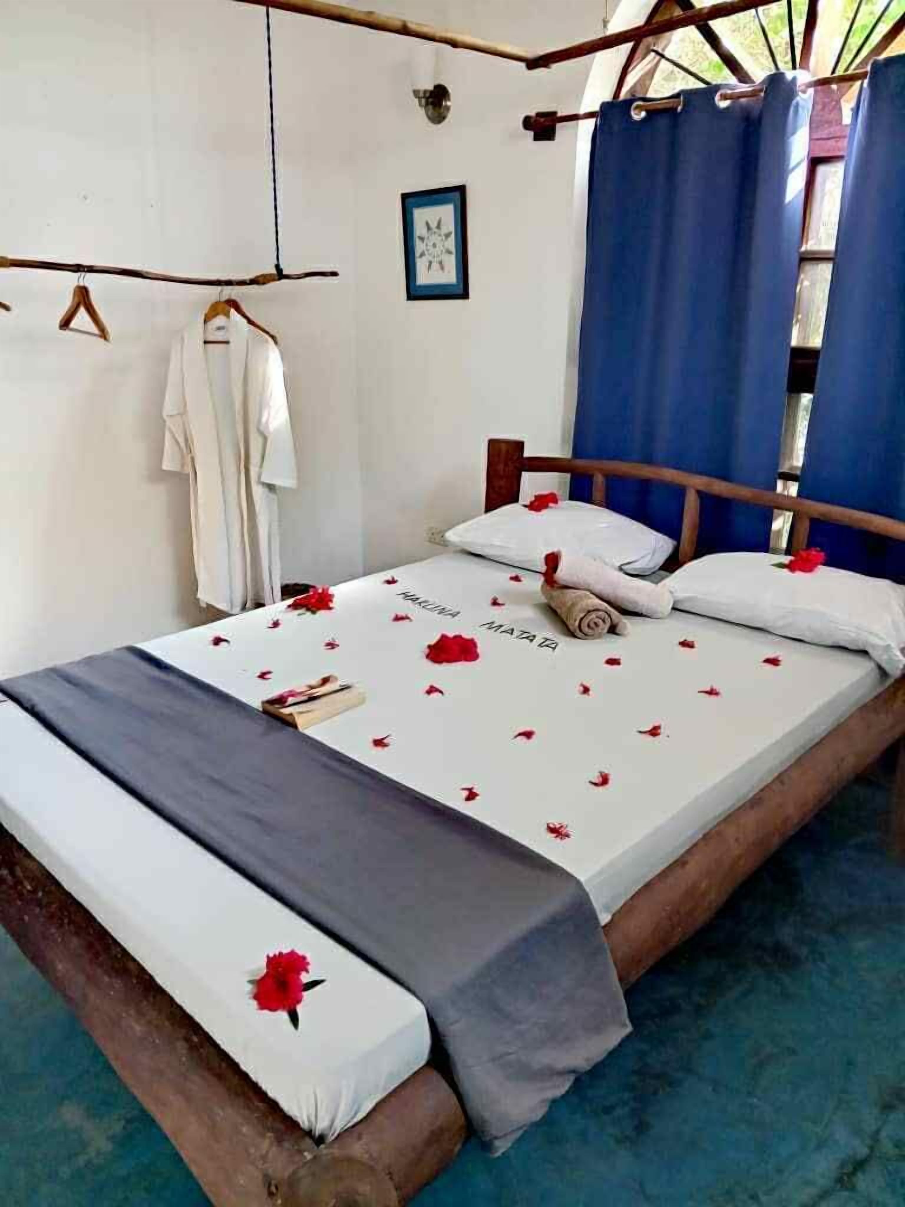 Een eenpersoonsbed met een witte matras, blauwe gordijnen en rode bloemen.
