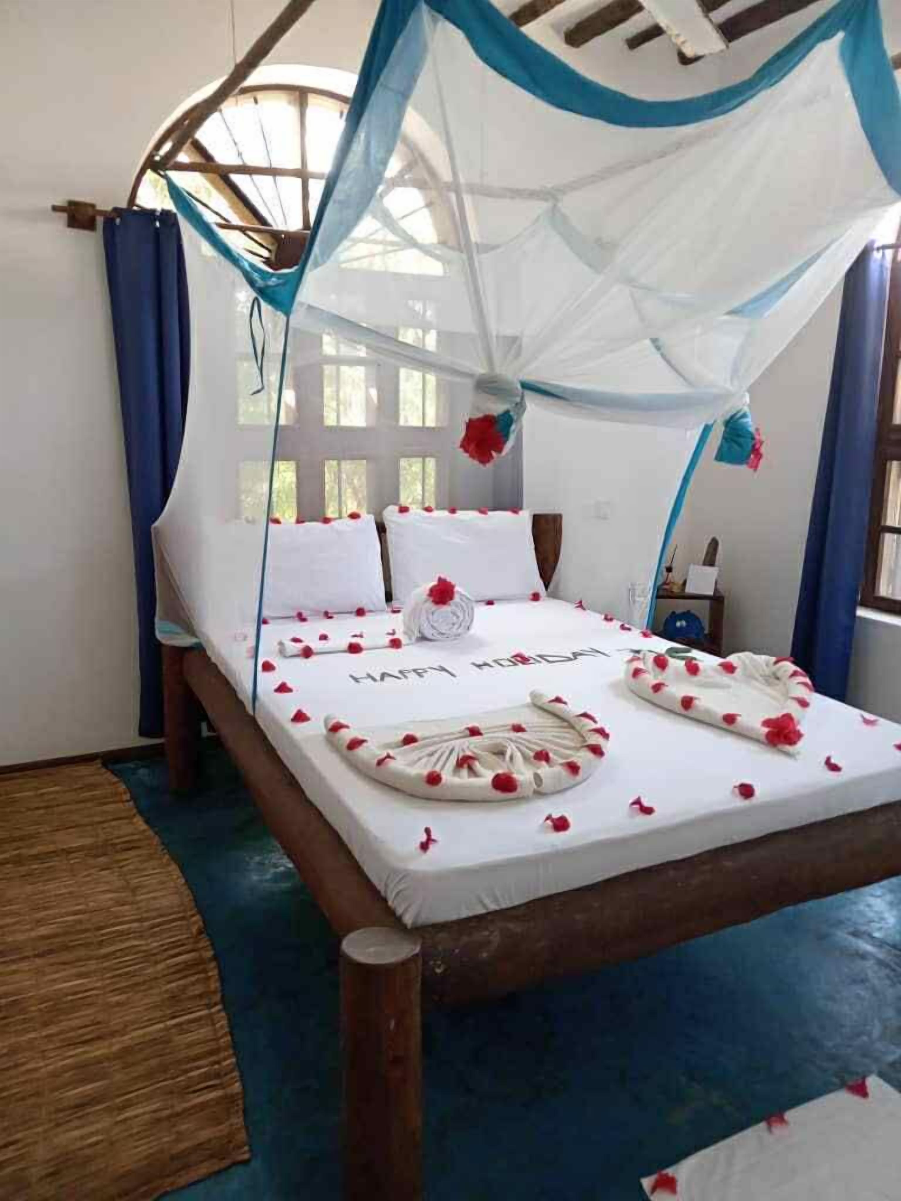 Una cama con dosel, ropa de cama blanca y pétalos de flores rojas.