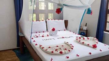 Una cama con dosel, ropa de cama blanca y pétalos de flores rojas.