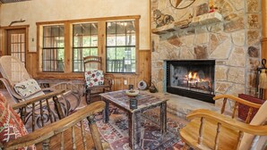 Una sala de estar acogedora con chimenea de piedra, muebles de madera y ventanas amplias.