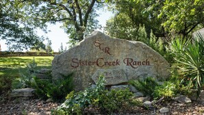 Un letrero de piedra grande con el texto “Sister Creek Ranch” y “Fundada en enero de 2002”, rodeado de follaje y árboles.