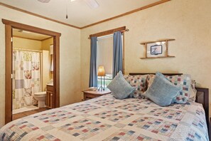 Ein Schlafzimmer mit gesteppter Bettdecke, einem Holz-Kopfteil, einem Nachttisch mit Lampe und einem gerahmten Bild an der Wand.
