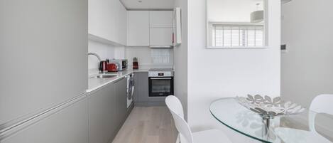 Une cuisine moderne avec des armoires blanches, un four encastré et une table à manger en verre, assortie de chaises.