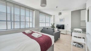 A modern hotel room with a large bed, a grey sofa, a glass table, and a TV. - Roomspace Apartments -Caroline Street (London)