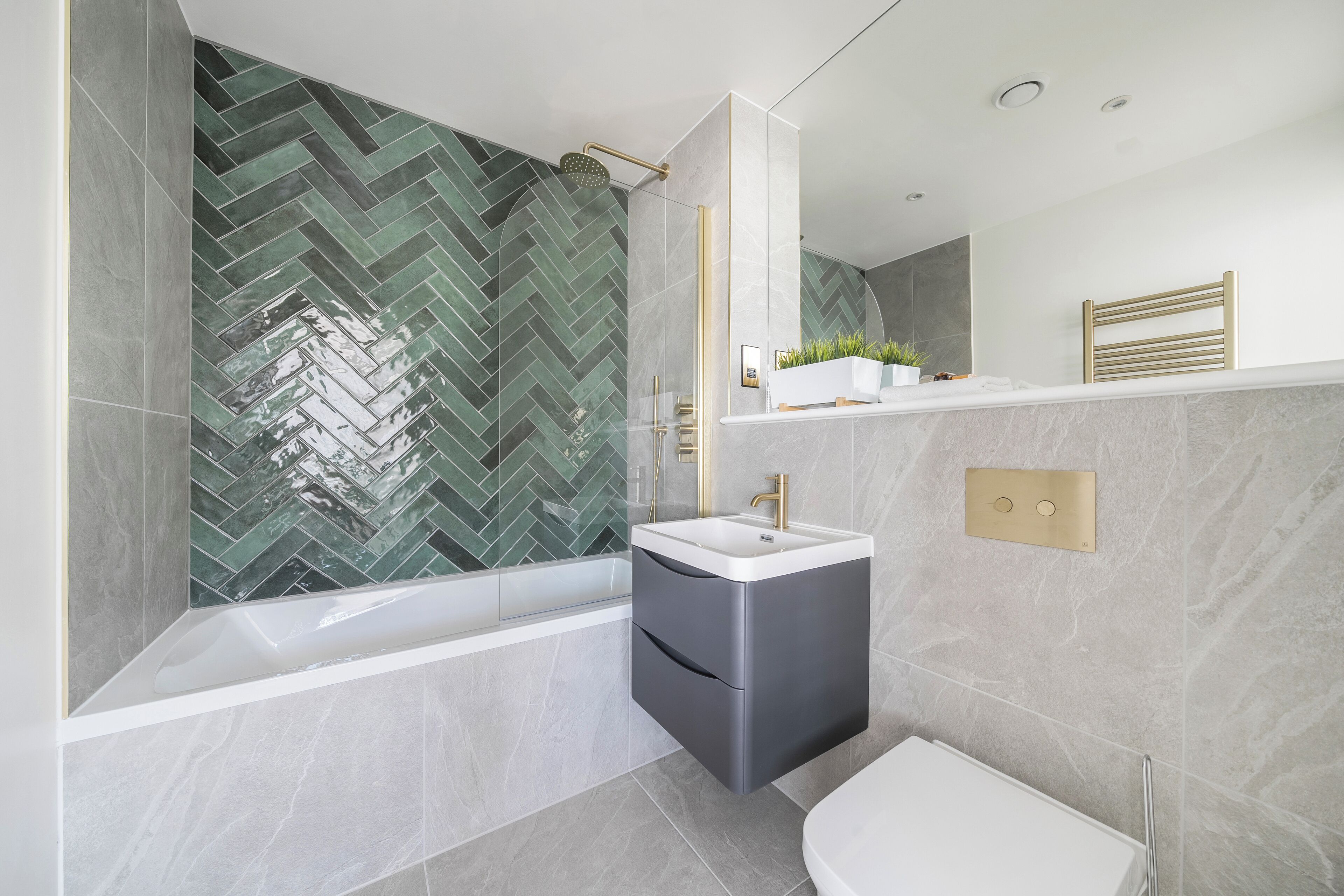 Un baño moderno con un resbalón de azulejos tipo espiga, una bañera independiente, un tocador con lavamanos y un inodoro.