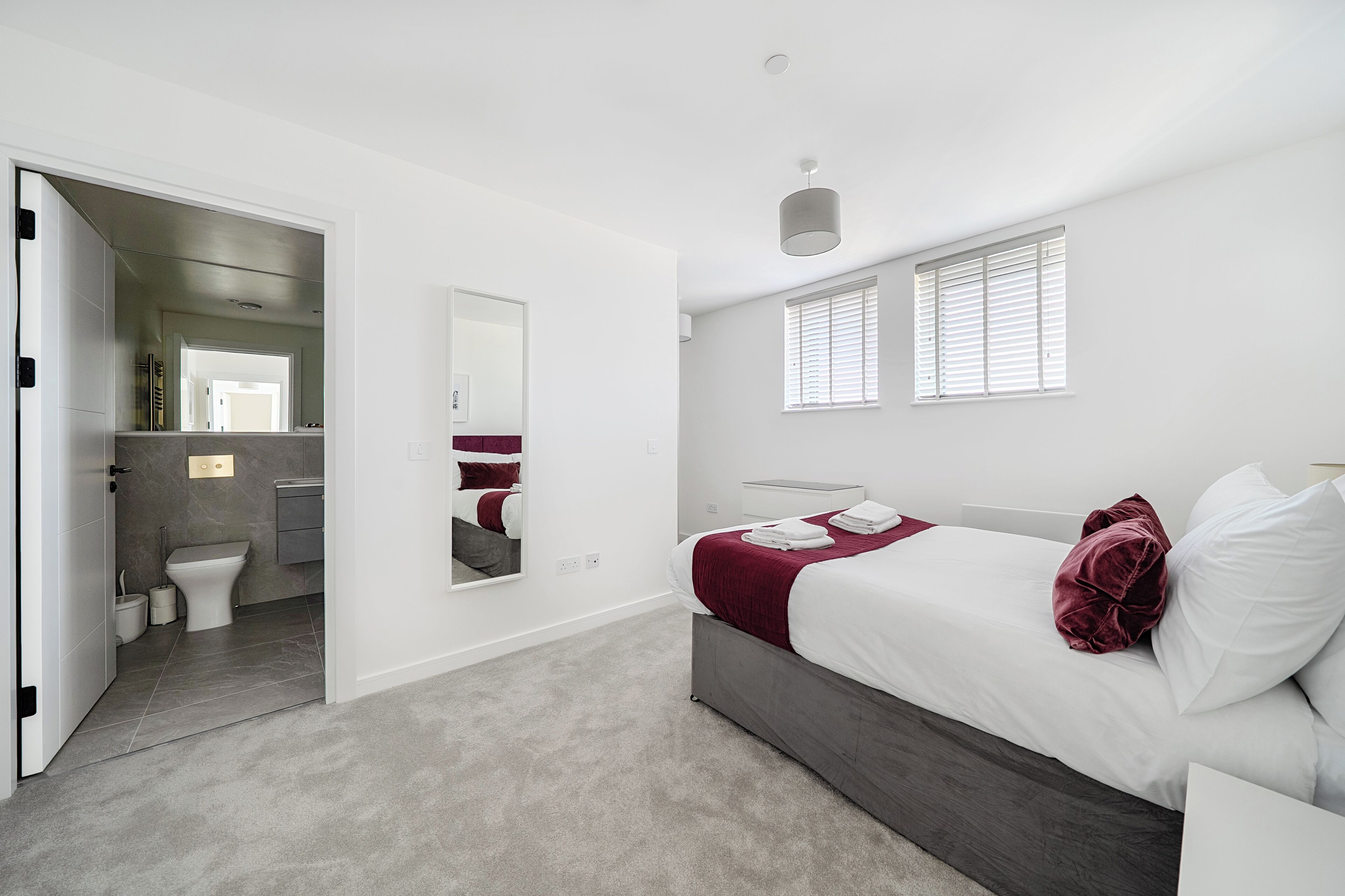 A modern bedroom with a large bed, a mirror, and a view of the bathroom.