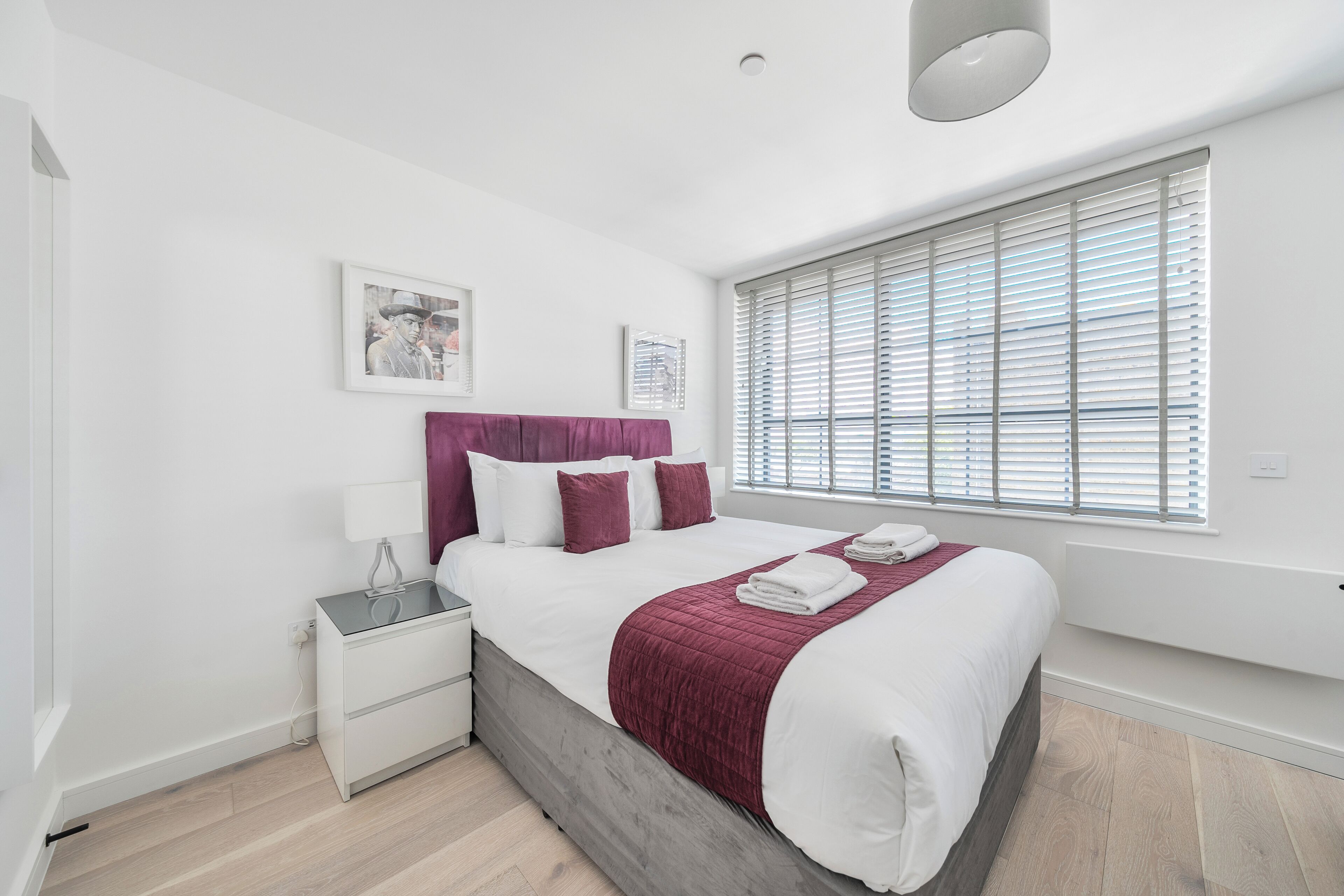 Un dormitorio moderno con una cama grande, paredes blancas y una ventana con persianas.