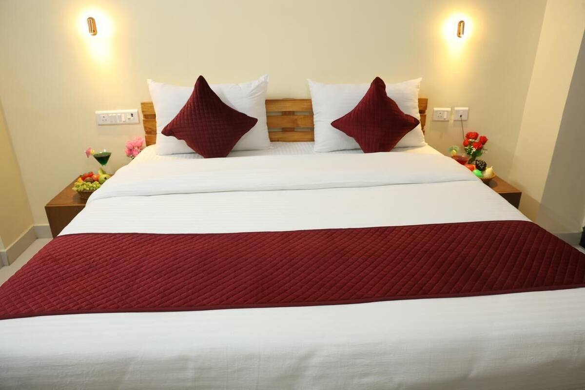 Cama bem arrumada com roupa de cama branca e vermelha, duas mesas de cabeceira com abajures e uma tomada na parede.