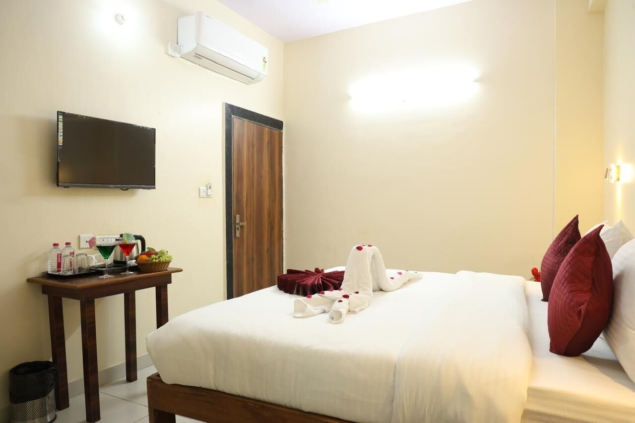 A hotel room with a bed, a TV mounted on the wall, a bedside table with toiletries, and a door.
