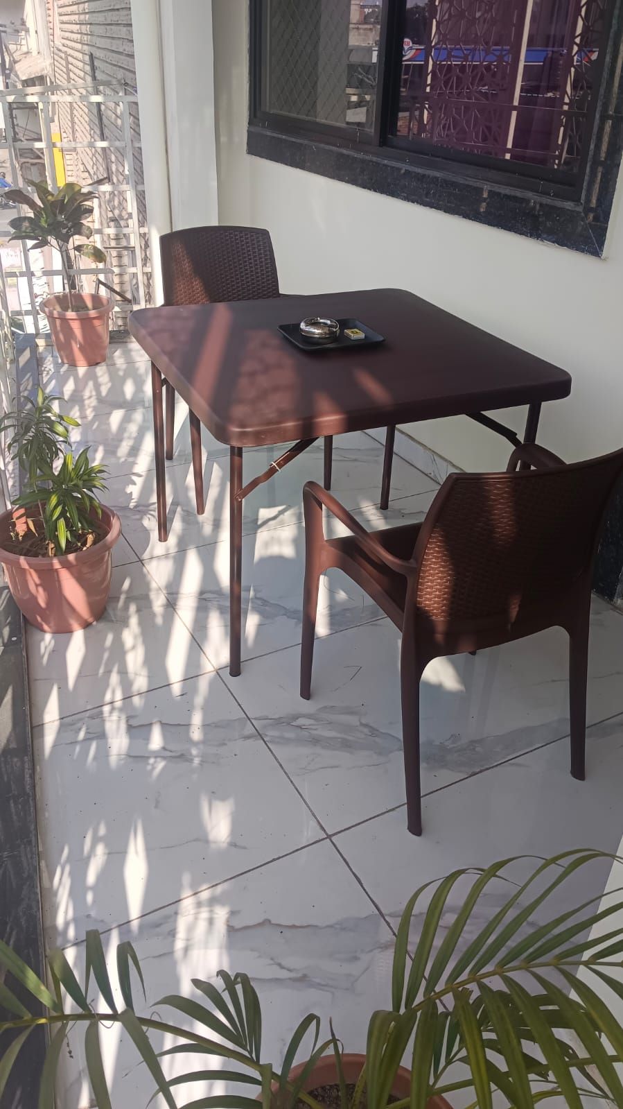 Un patio con mesa y sillas, plantas en macetas y una ventana con vistas a edificios.