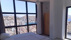 A bedroom with a large bed, a wooden wardrobe, and a view of a cityscape through large windows. - Brian's Rooms (Sarande)