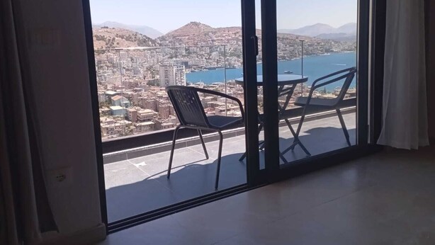 A balcony with a table and chairs, overlooking a cityscape and a body of water. - Brian's Rooms (Sarande)