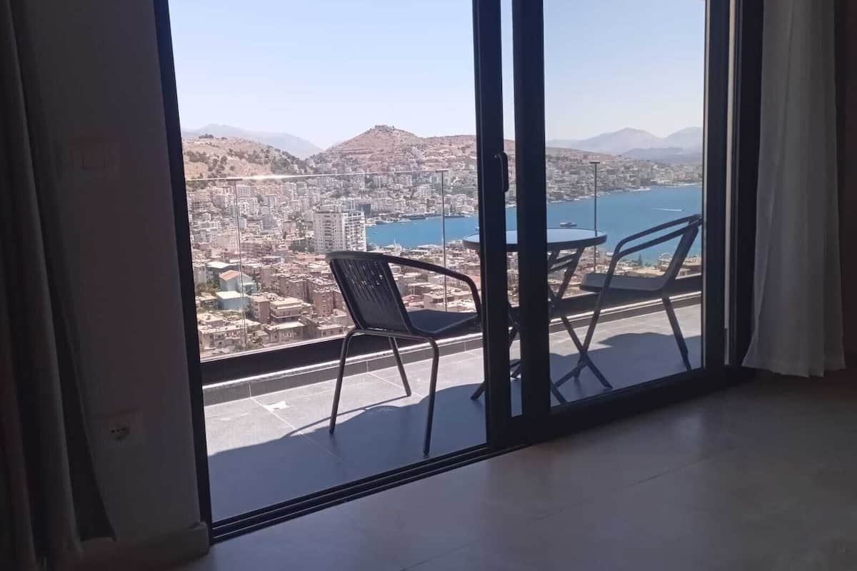 A balcony with a table and chairs, overlooking a cityscape and a body of water.