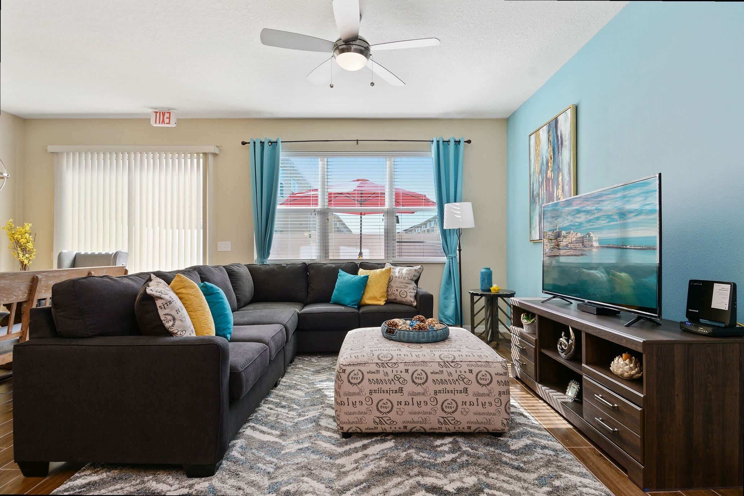 A living room with a sectional sofa, a flat-screen TV, and a ceiling fan.
