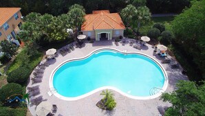 Ein Pool mit Liegestühlen und Sonnenschirmen, umgeben von Palmen und einem Gebäude mit einem Kacheldach.